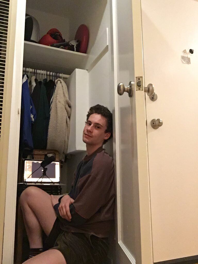 a man sitting in a closet with a laptop and microphone