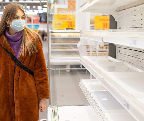 woman in a grocery store wearing a mask looking at empty shelv es