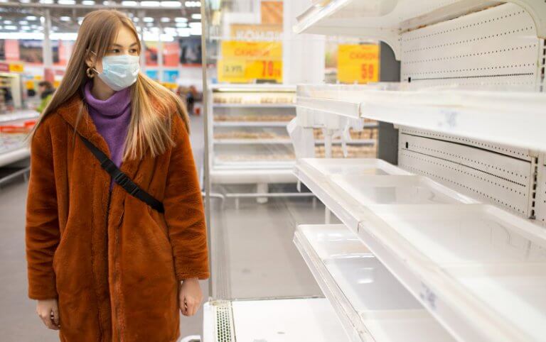 woman in a grocery store wearing a mask looking at empty shelv es